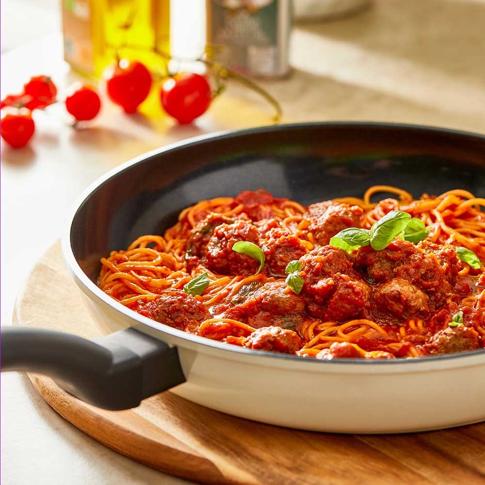 A 32-cm Baccarat  Bio Frying pan containing pasta on a wooden board surrounded by fresh ingredients