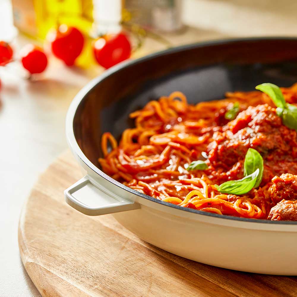 A 32-cm Baccarat  Bio Frying pan containing pasta on a wooden board surrounded by fresh ingredients