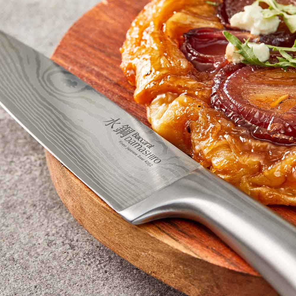 Close-up of Baccarat Damashiro Satori kitchen knife with a patterned blade on a grey countertop 