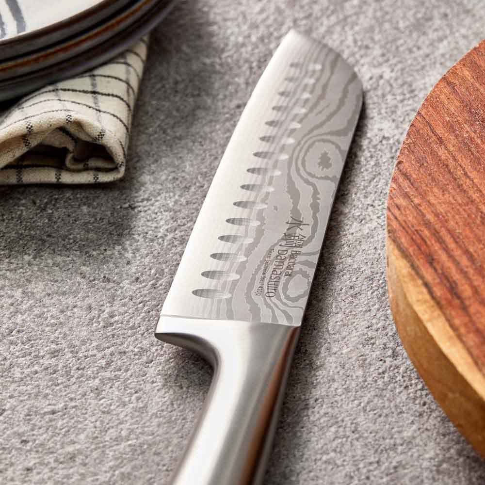 Close-up of Baccarat Damashiro Satori kitchen knife with a patterned blade on a grey countertop 