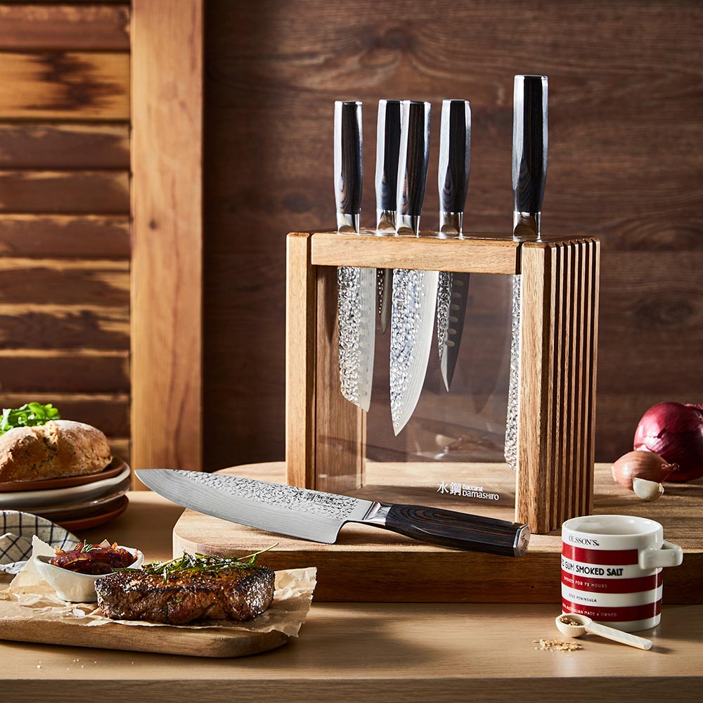 Person slices steak on a wooden board wearing blue-striped apron ideal for kitchen tasks - Baccarat