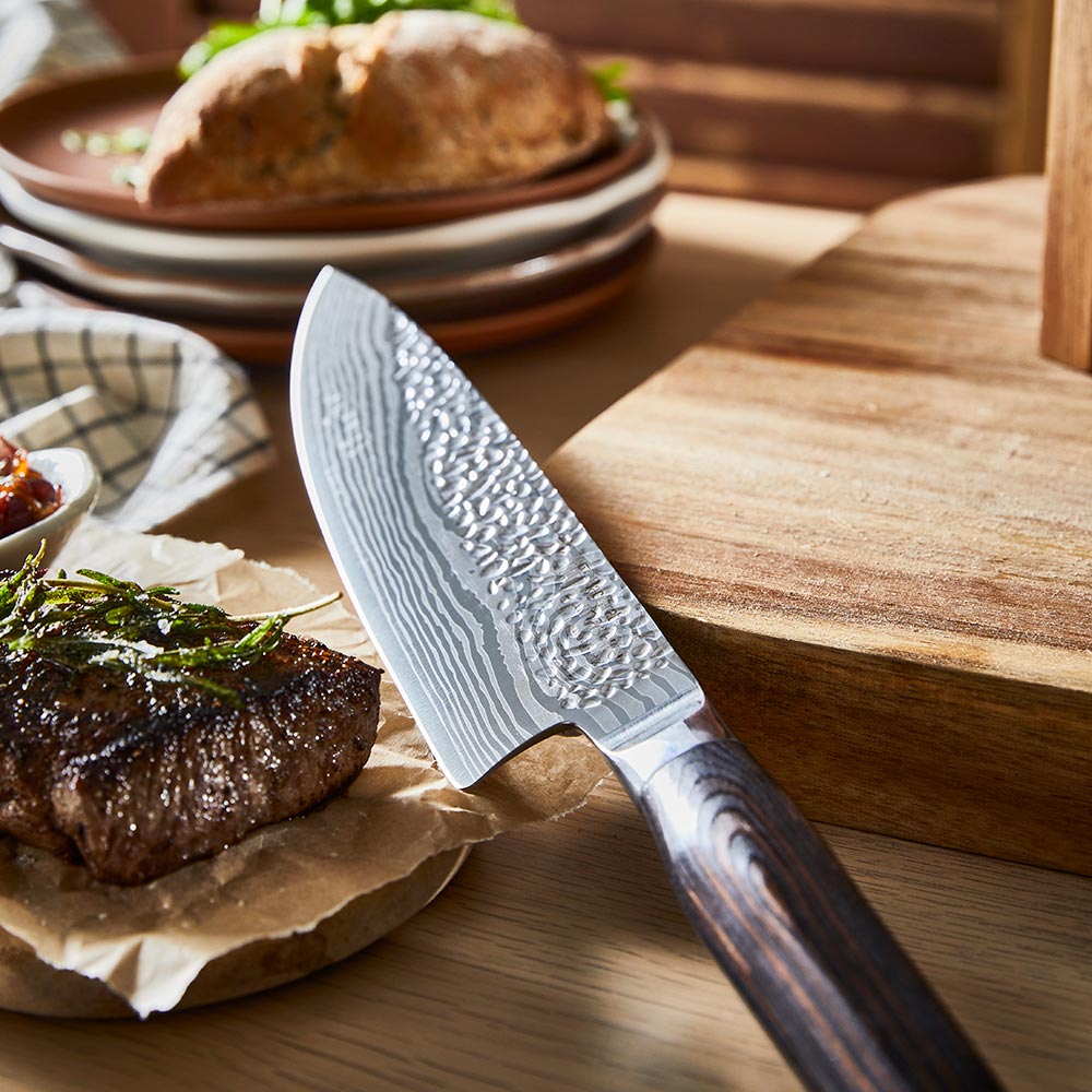 Person slices steak on a wooden board wearing blue-striped apron ideal for kitchen tasks - Baccarat