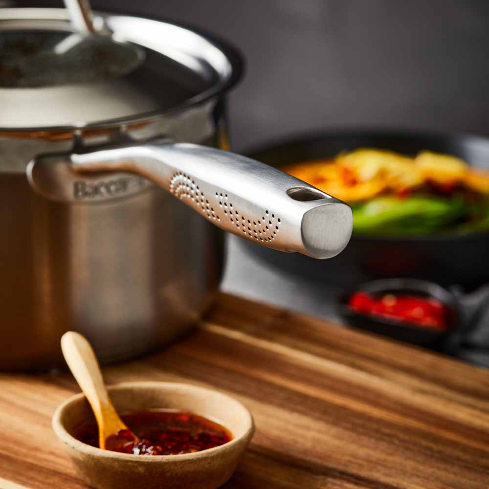 stainless steel saucepan 20cm pot of soup on a wooden board beside black bowl of noodles  - Baccarat