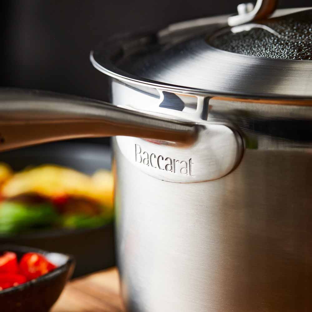 stainless steel saucepan 20cm pot of soup on a wooden board beside black bowl of noodles  - Baccarat