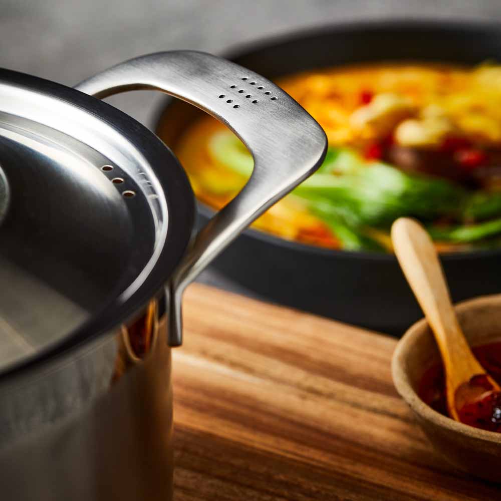 stainless steel saucepan 20cm pot of soup on a wooden board beside black bowl of noodles  - Baccarat