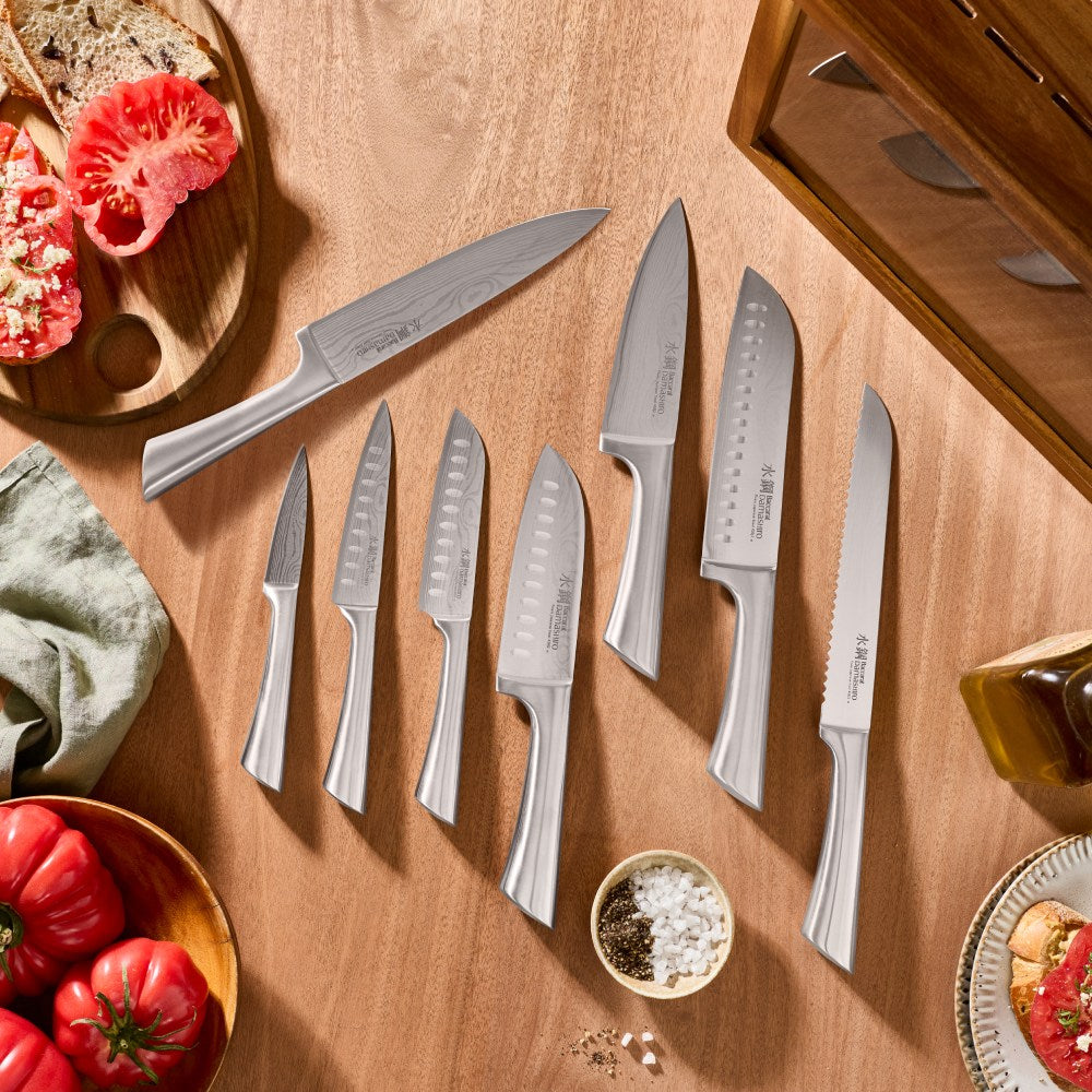 Set of knives on a wooden surface with vegetables and a cutting board.