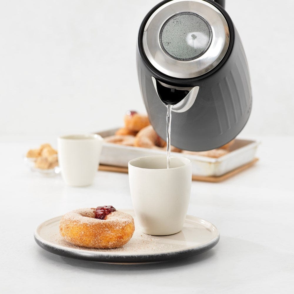 Black kettle pours hot water into a white cup beside a pastry plate - Baccarat  Boiling Point Kettle