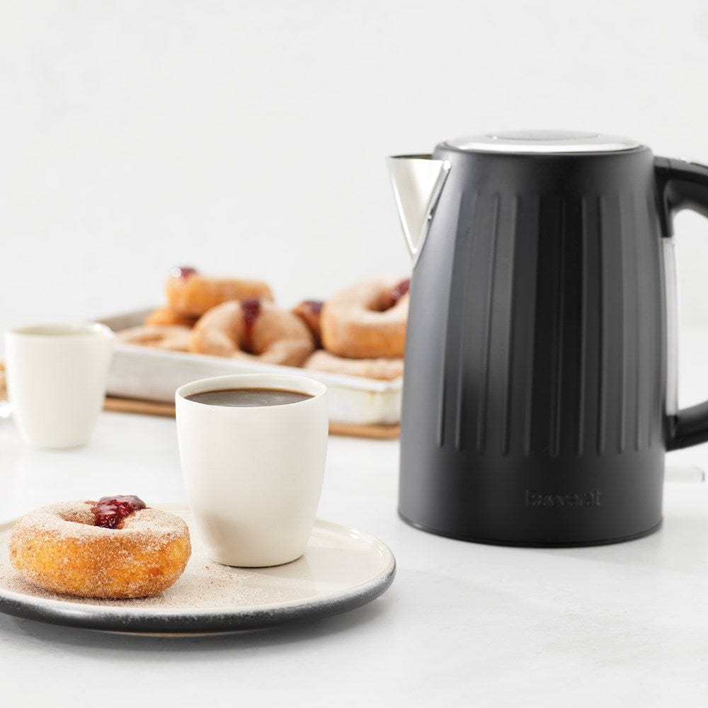 Black kettle pours hot water into a white cup beside a pastry plate - Baccarat  Boiling Point Kettle